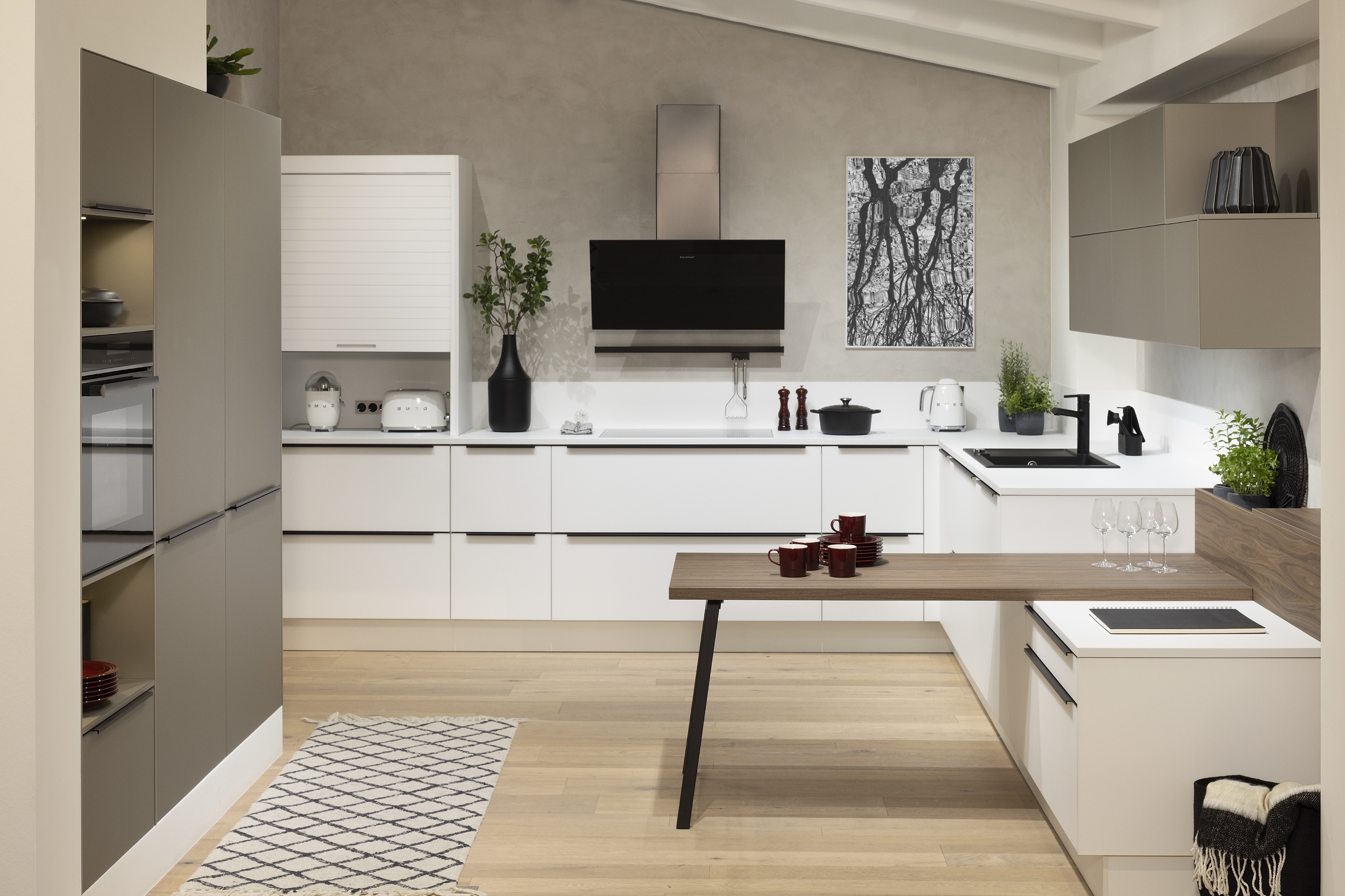 APL: 159 Kristallweiß 25 mm + 140 Walnuss-natur Repro 40 mm (Tisch) Front: SMART Kristallweiß Polymerglas + Farbe Sandgrau metallic Korpus: 4077 Kristallweiß Griff: M745 Schwarz matt Geräte: Blaupunkt Armatur: Franke Spüle: Franke  Features: Oberfläche Polymerglas, Tischlösung, Stauraum mit Rollo, Kopffreihaube, LeMans Schrank für die Ecke, Küche für die Dachschräge, 