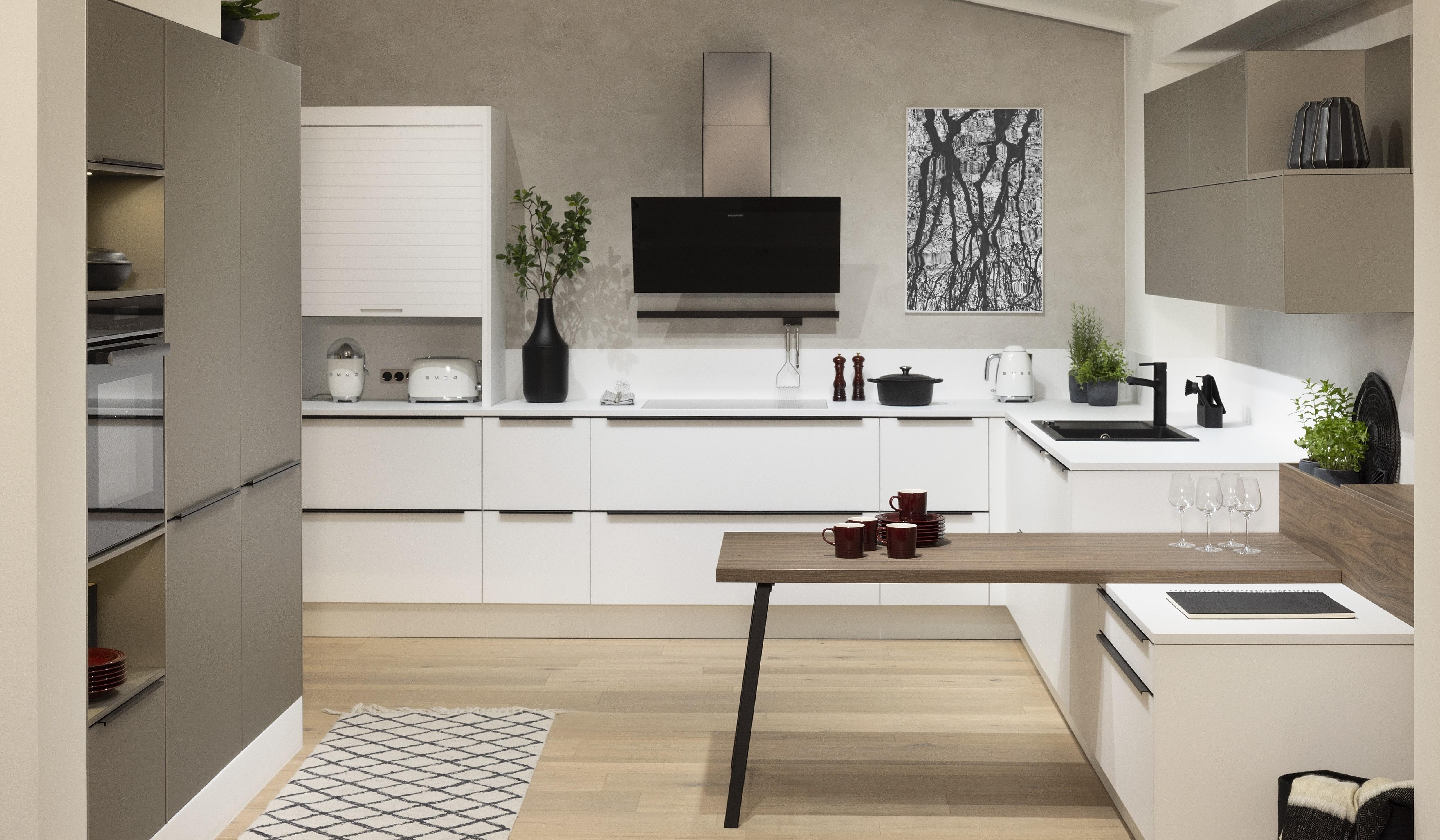 APL: 159 Kristallweiß 25 mm + 140 Walnuss-natur Repro 40 mm (Tisch) Front: SMART Kristallweiß Polymerglas + Farbe Sandgrau metallic Korpus: 4077 Kristallweiß Griff: M745 Schwarz matt Geräte: Blaupunkt Armatur: Franke Spüle: Franke  Features: Oberfläche Polymerglas, Tischlösung, Stauraum mit Rollo, Kopffreihaube, LeMans Schrank für die Ecke, Küche für die Dachschräge, 