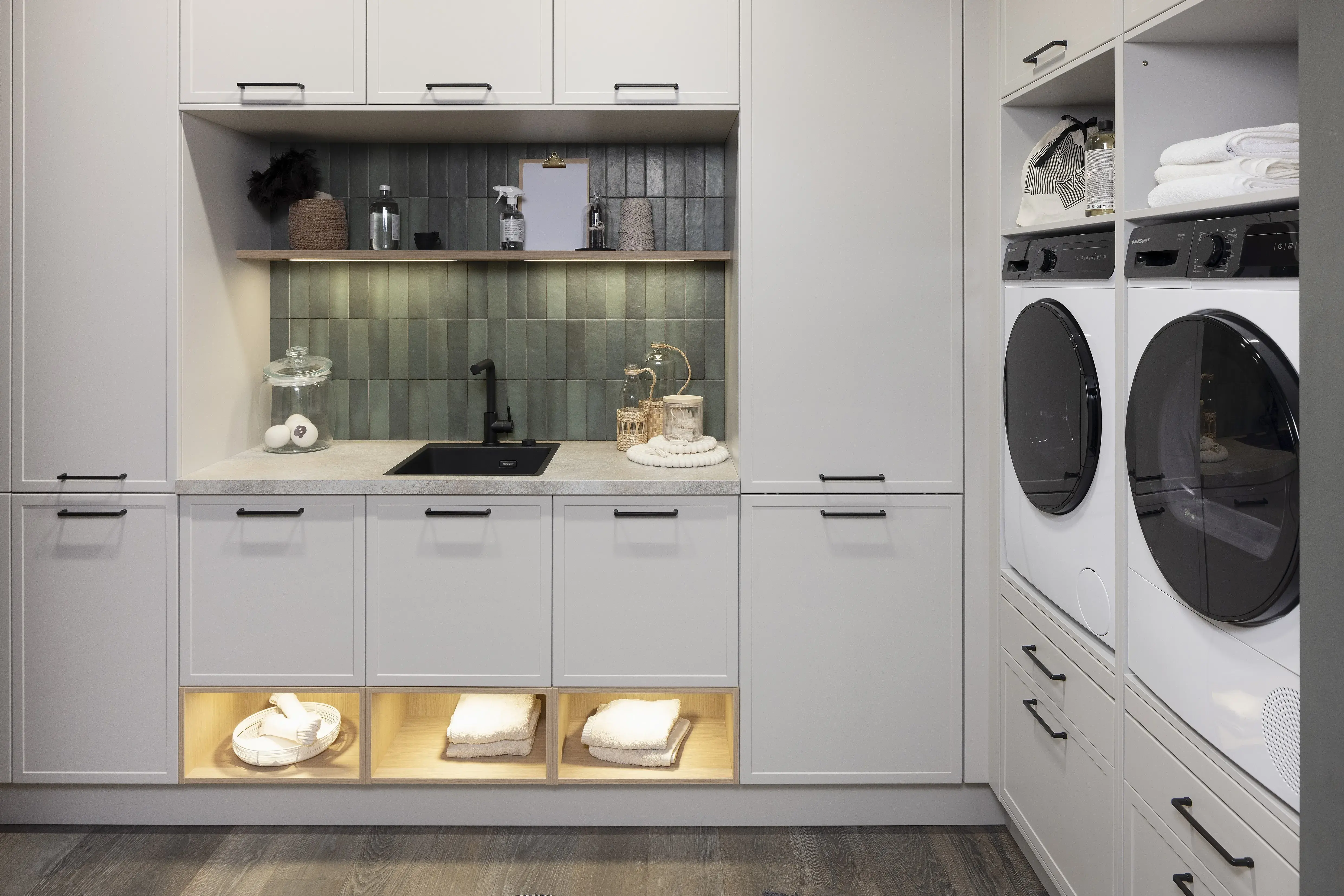 APL: 15 Kalkstein Repro 40 mm Front: AV 5085 Mattlack Sandgrau (RAL + NCS) Korpus: 2022 Designkorpus Lichtgrau bzw. 2085 Designkorpus Feineiche-natur Griff: 505 Metall Schwarz-matt Geräte: Blaupunkt Armatur: Blaupunkt Spüle: Blaupunkt  Features: HWR, Waschmaschine und Trockner ergonomisch eingebaut, Fliesen, Wein-/Flaschenregal, 